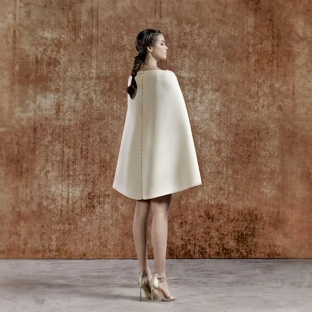 Beige crepe short dress with a v shape embriodered neckline. Long sleeves with attached cape and back buttoning.