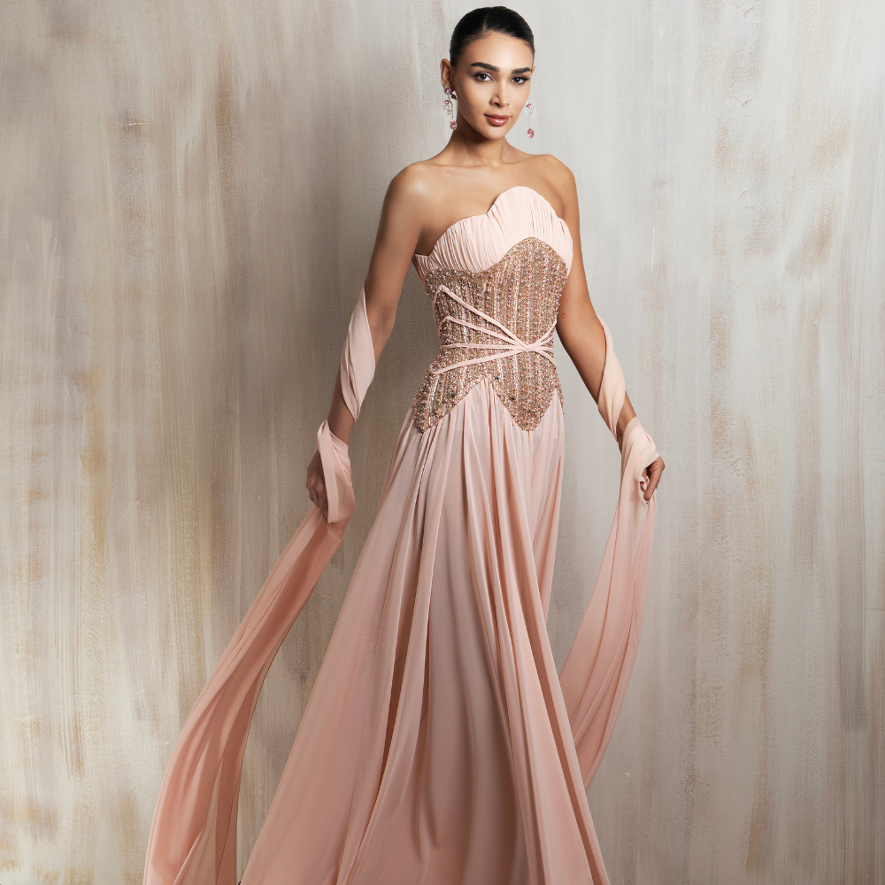 Blush strapless gown with an embellished corset, pleated chiffon skirt, and flowing draped sleeves. Shop now at our exclusive clothing website.