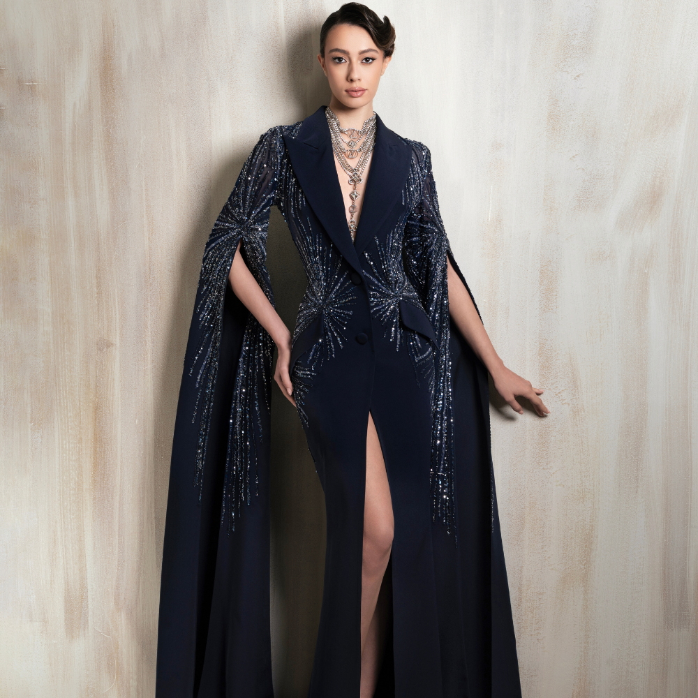 Navy tailored gown with a blazer-style bodice, deep neckline, high slit, and sequined cape sleeves. Shop now at our exclusive clothing website.