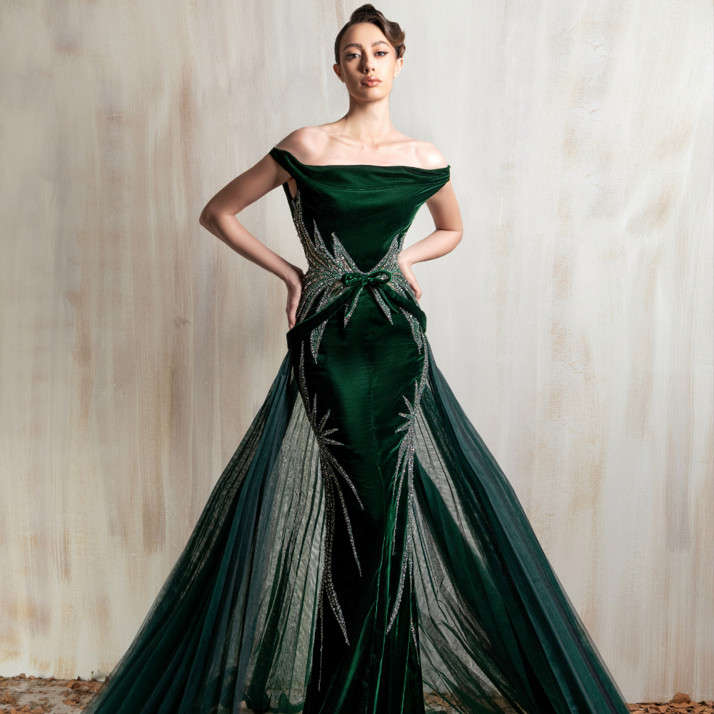 Off-shoulder deep emerald gown with crystal waist detailing, sheer tulle panels, and a flowing train. Shop now at our exclusive clothing website.