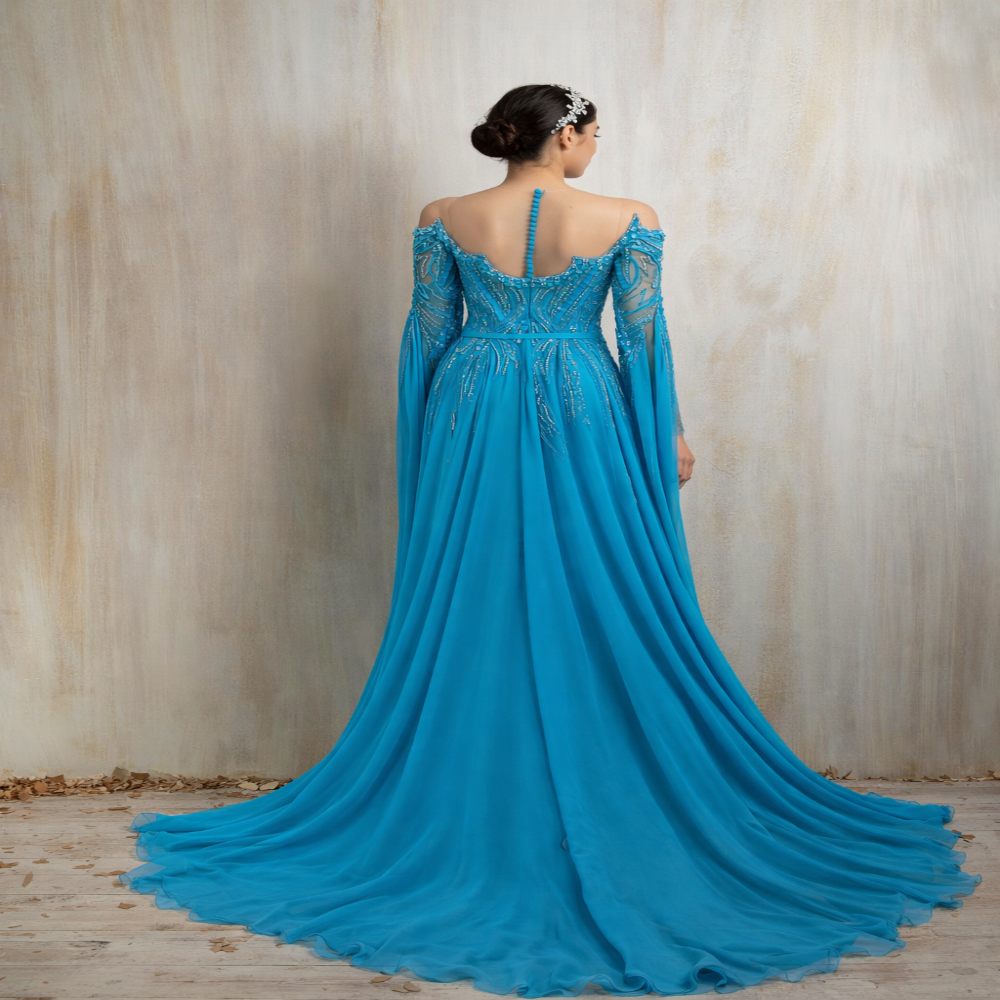 Turquoise embellished gown with a graceful flowing cape, designed for elegant evening occasions. Shop now at our exclusive clothing website.