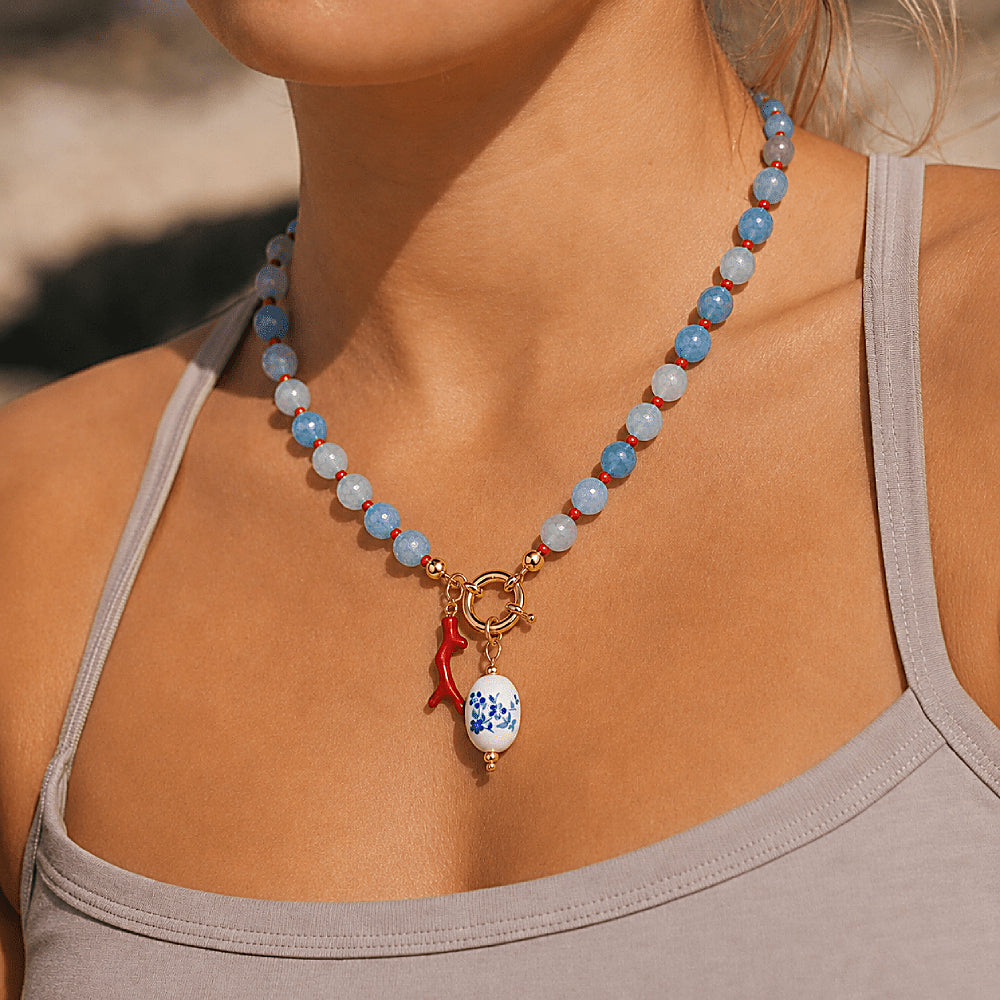 Discover the Azure Reef Agate Beaded Necklace at The Luxe Maison, featuring blue agate beads, vibrant red accents, a coral branch charm, and a blue-and-white porcelain bead for a playful, ocean-inspired look.