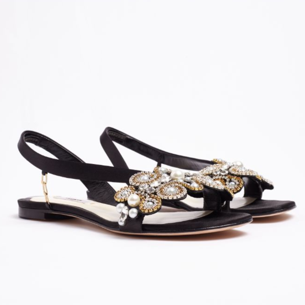 The L’Amazone Mon Bijoux flat sandal is designed in rich black double satin adorned with embellishments at its toe band.