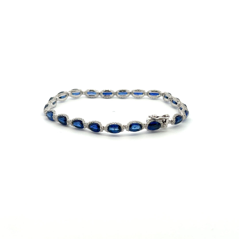 Sterling silver rhodium plated tennis bracelet featuring oval lab-created blue sapphires surrounded by sparkling cubic zirconia for a timeless statement look. Shop premium jewelry online.