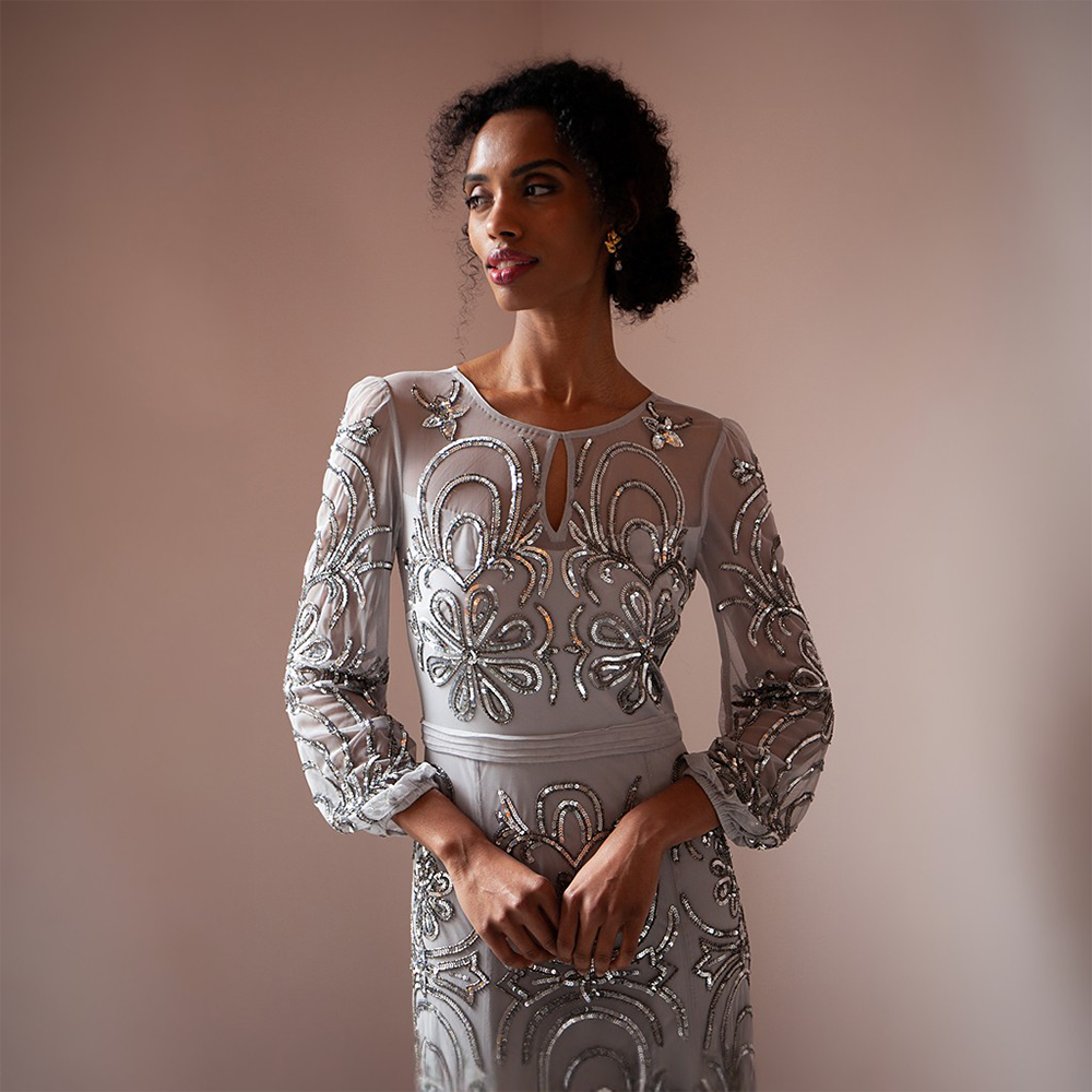 Elevate your look with the breathtaking silver floor-length gown adorned featuring mesh sleeves and a neckline.