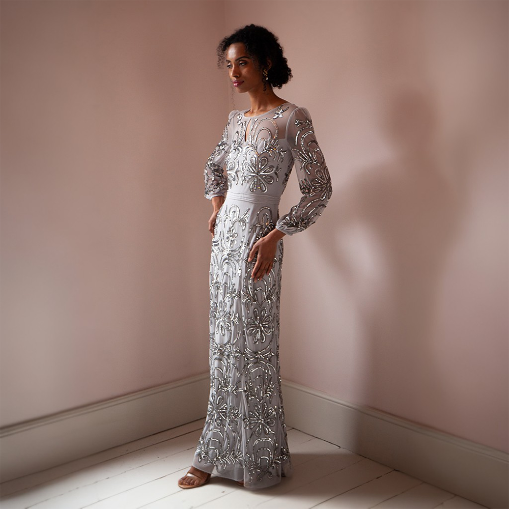 Elevate your look with the breathtaking silver floor-length gown adorned featuring mesh sleeves and a neckline.