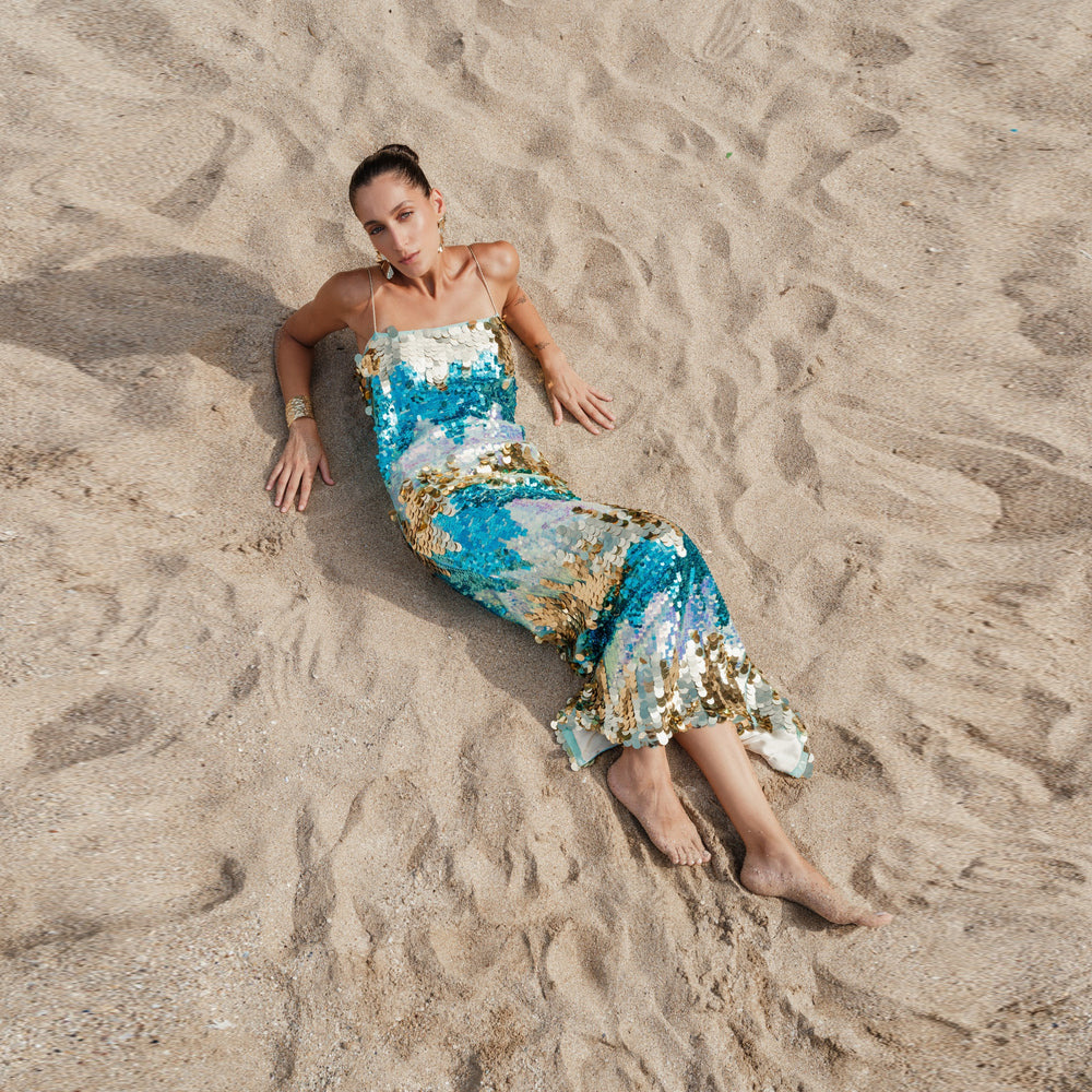 Shop online from our exclusive website and discover the Dila Dress by Nana Gotti, featuring turquoise and gold sequins with a collarbone-baring silhouette for elegant statement style.