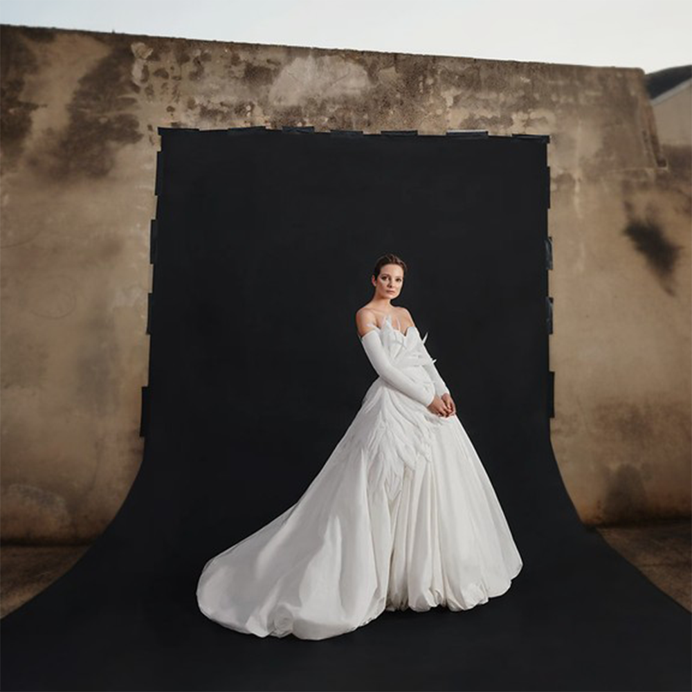 Off-the-shoulder ivory silk taffeta puffball wedding gown featuring plumes emerging at the side waist.