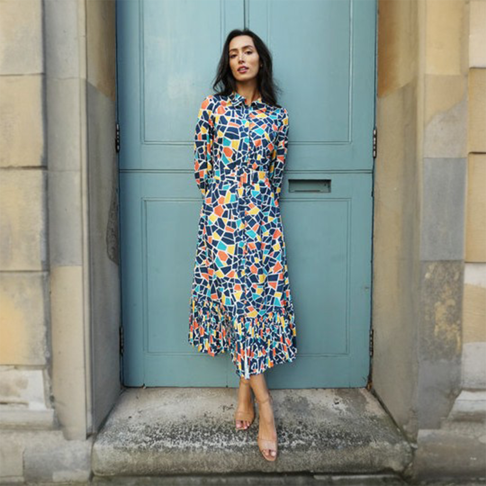 Vibrant blue, yellow and orange geometric print dress has a buttoned front and a buckled belt finished with a pleated hem