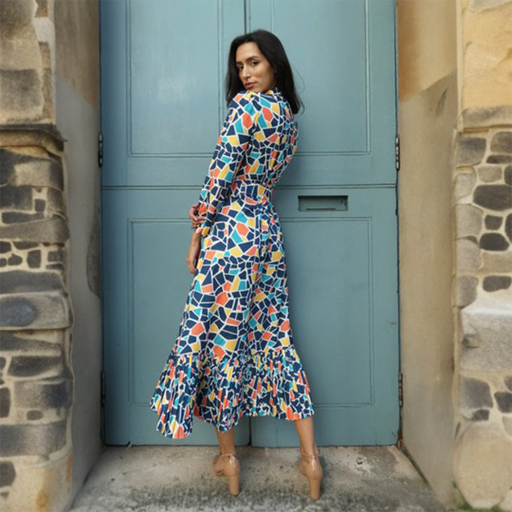 Vibrant blue, yellow and orange geometric print dress has a buttoned front and a buckled belt finished with a pleated hem