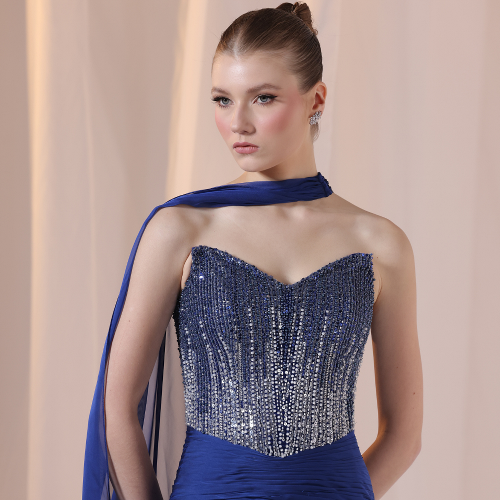 Shop online deep blue gown with one-shoulder silhouette, rich embellishments and flowing sheer drape, perfect for parties and special occasions.