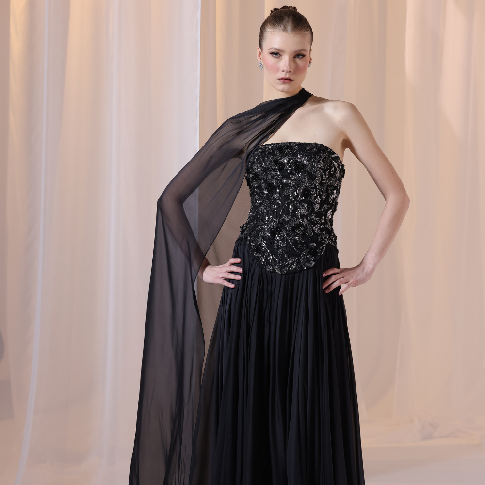 Shop online black gown with embellished strapless bodice, flowing silhouette and sheer one-shoulder drape, perfect for parties and special occasions.