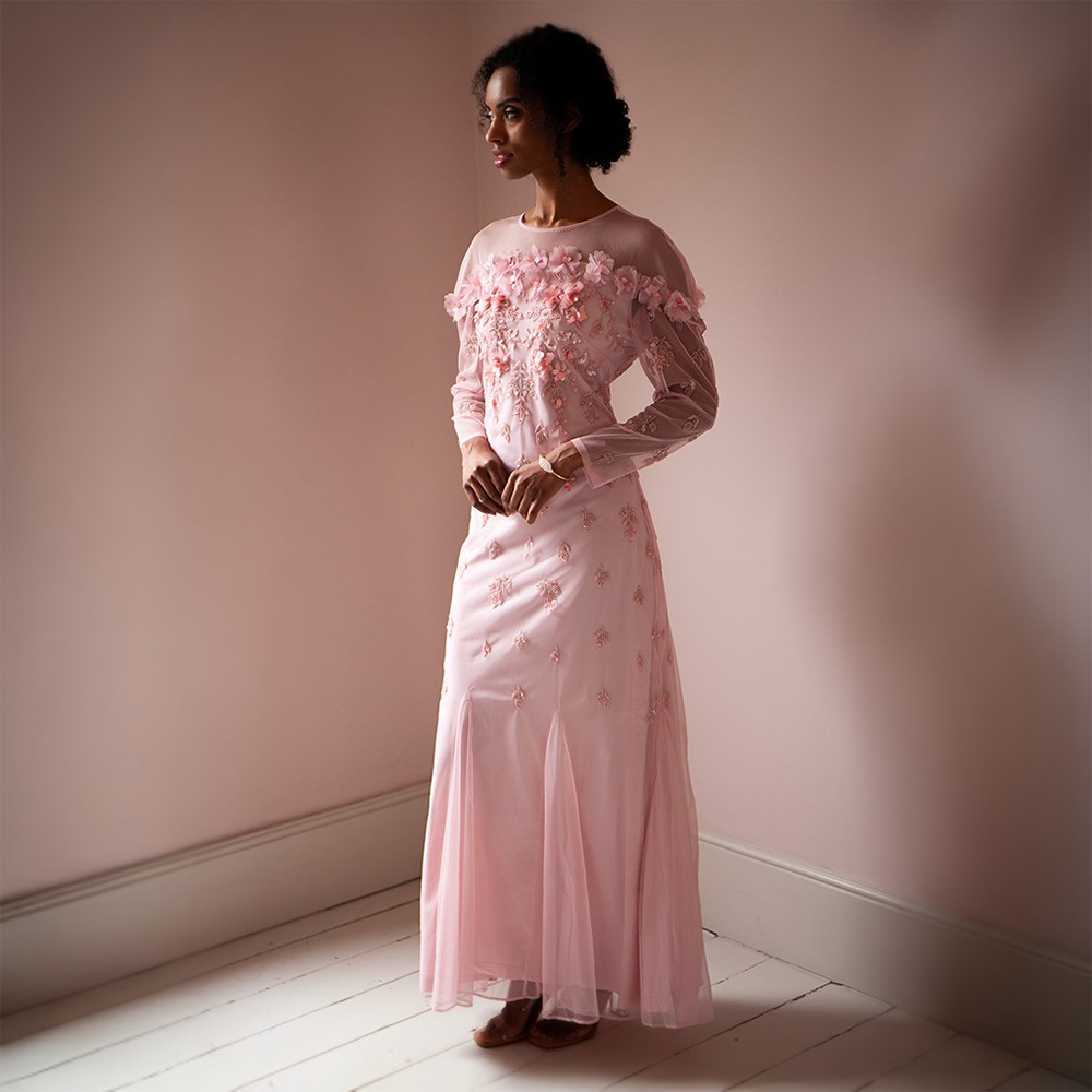 The Maddy Gown is floor length with a sheer neckline and full-length sheer sleeves.