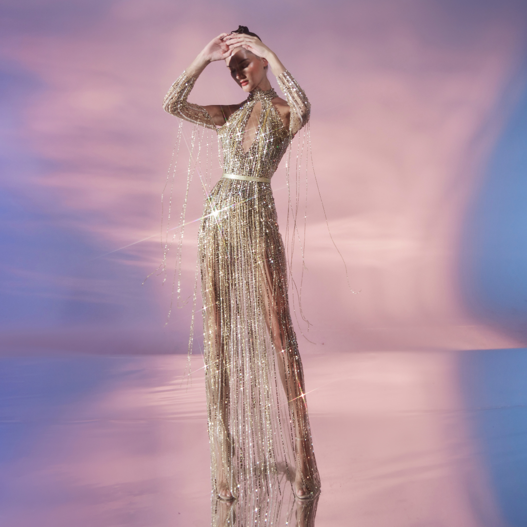 The long-sleeved Nude tulle sheath dress is fully embellished in Gold sequins and stones featuring fringe detail.
