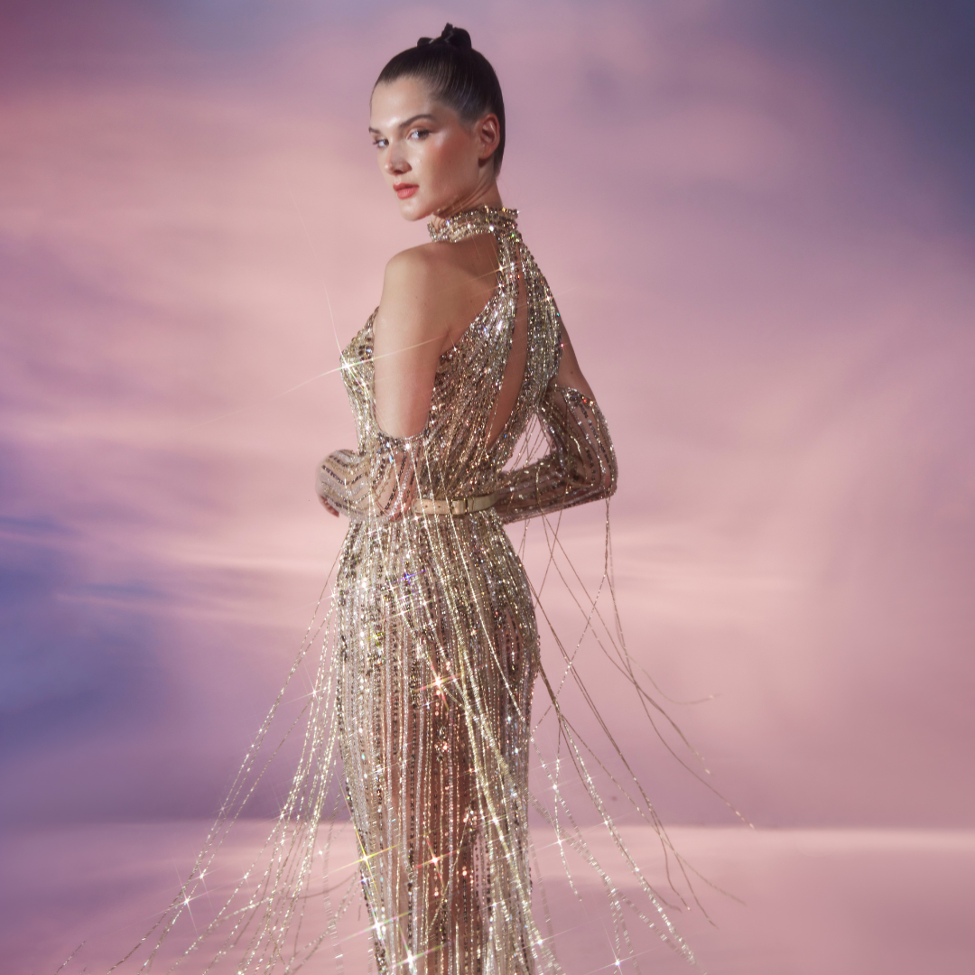 The long-sleeved Nude tulle sheath dress is fully embellished in Gold sequins and stones featuring fringe detail.