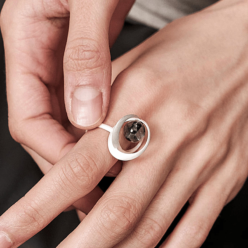 Discover the Orbit Black Rutilated Quartz & Sterling Silver Ring at The Luxe Maison, featuring a unique natural quartz sphere with star-like black rutile inclusions, framed by sculptural S925 sterling silver curves. Inspired by celestial motion, this distinctive ring combines contemporary elegance with cosmic charm.
