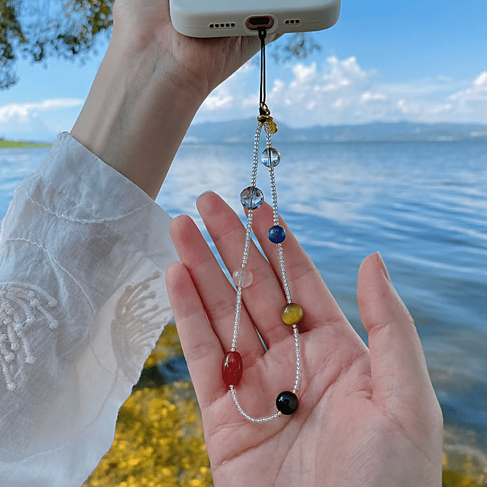 Discover the Seven Chakras Gemstone Phone Strap at The Luxe Maison, featuring natural crystals, golden accents, and a lucky charm for a colorful, celestial-inspired accessory.