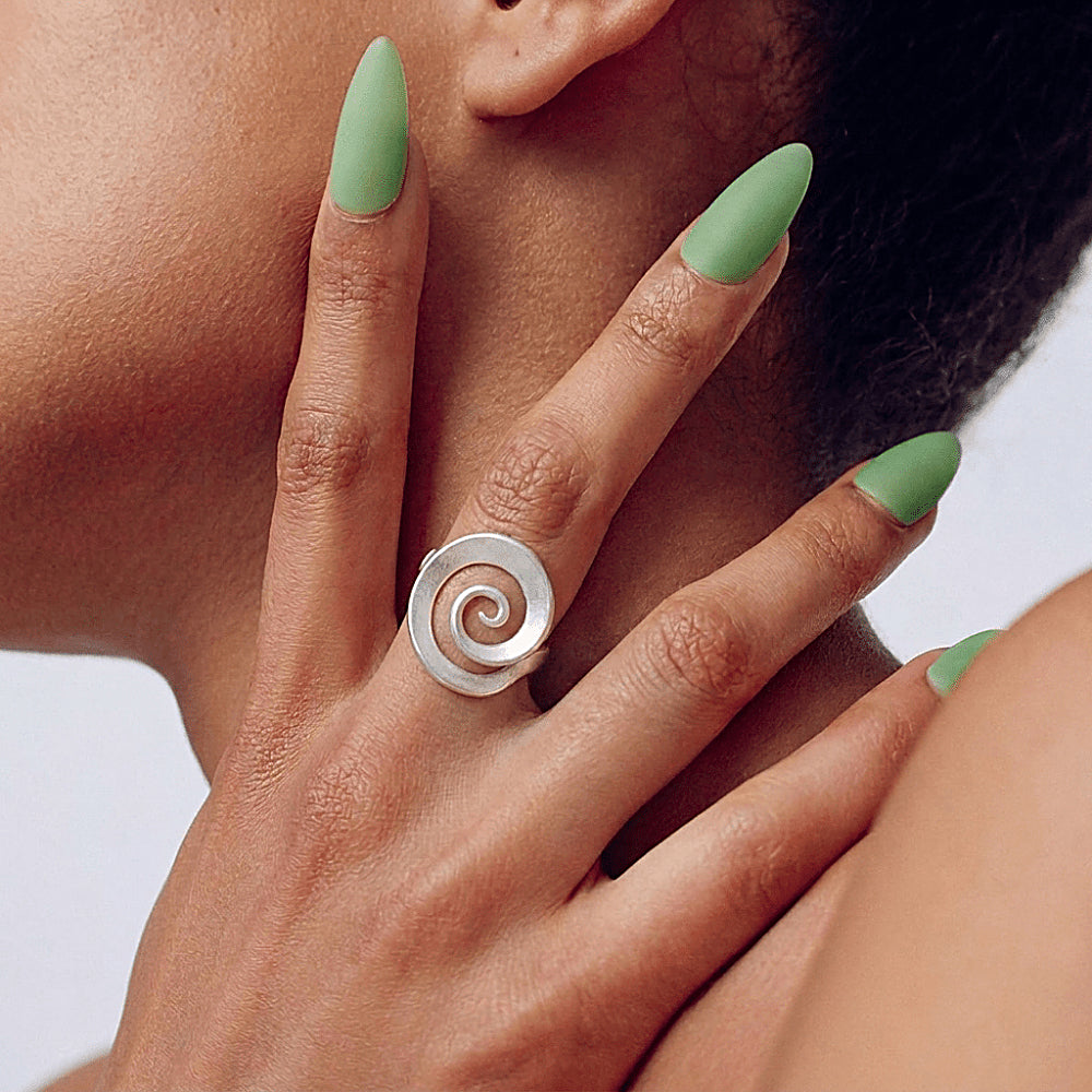 Discover the Vortex Sterling Silver Spiral Ring at The Luxe Maison, featuring a sculptural spiral design and a softly matte sterling silver finish. Inspired by the flowing forms of nature and the cosmos, this adjustable statement ring combines contemporary elegance with organic movement, making it perfect for everyday wear and special occasions.