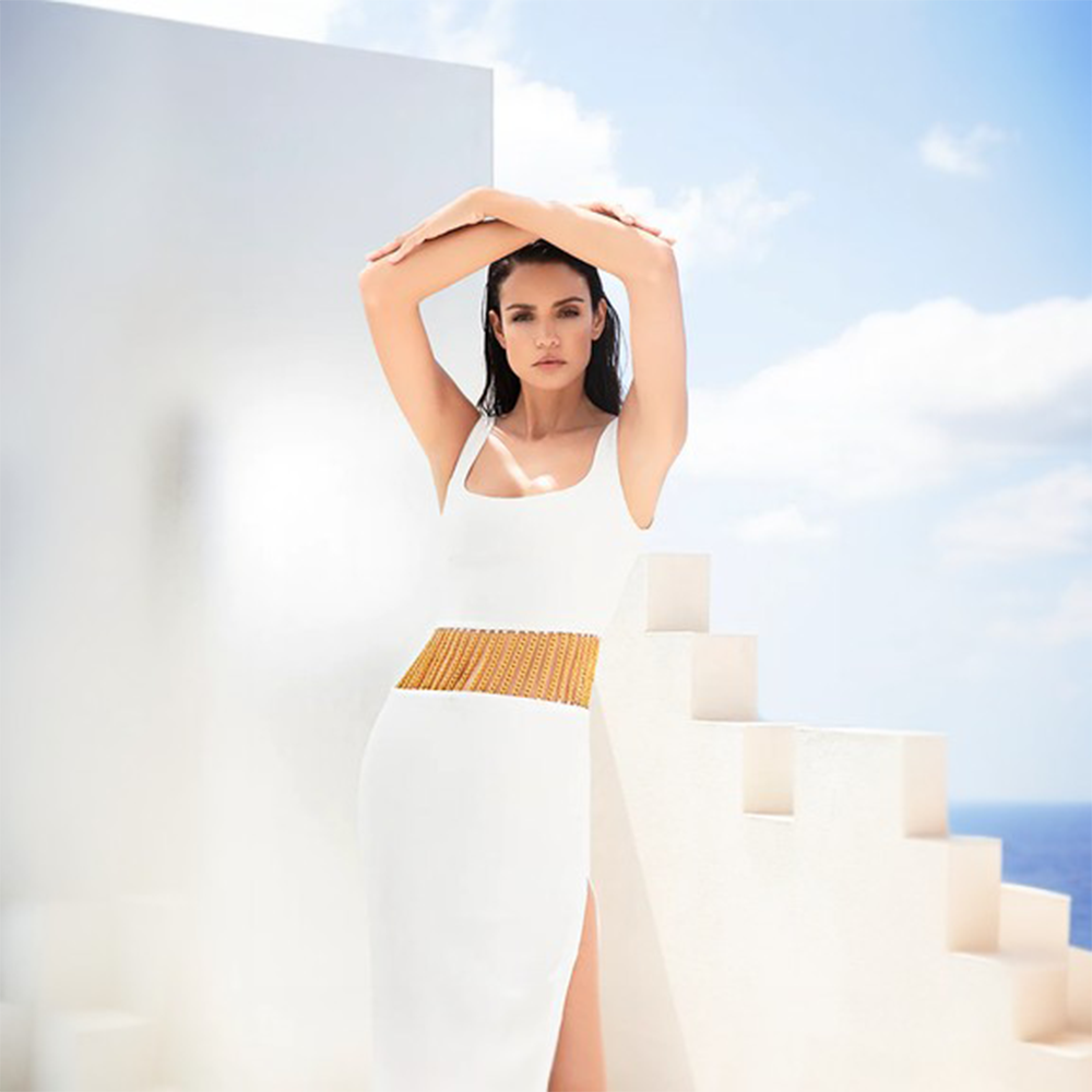 A white silk crepe dress with a thigh-high side slit and gold chain detailing at the waistline.