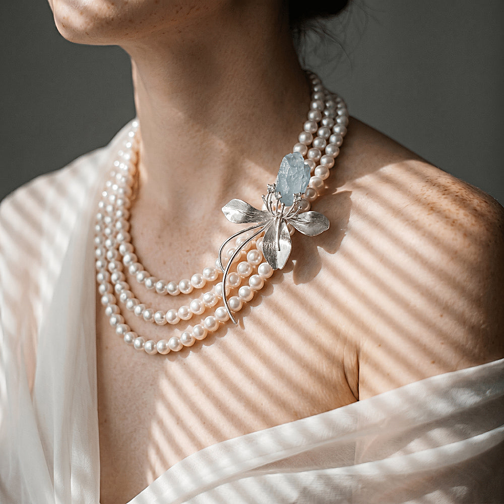 Discover the Wild Iris Silver & Aquamarine Brooch at The Luxe Maison, featuring a raw aquamarine crystal set in sculptural silver petals, with a versatile design that can also be worn as a pendant.