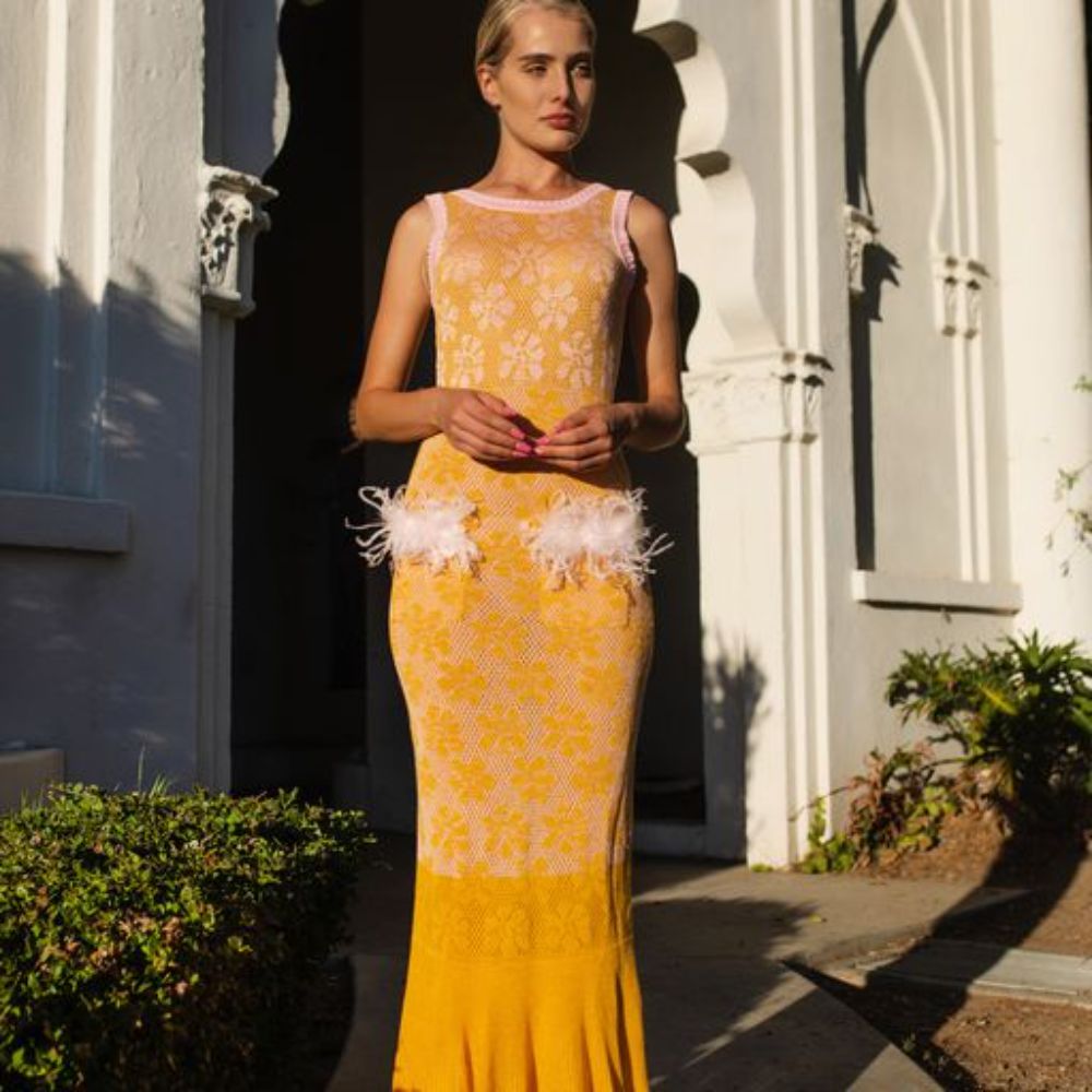 Yellow knit dress is designed with a round neck and feathers on the pockets. 