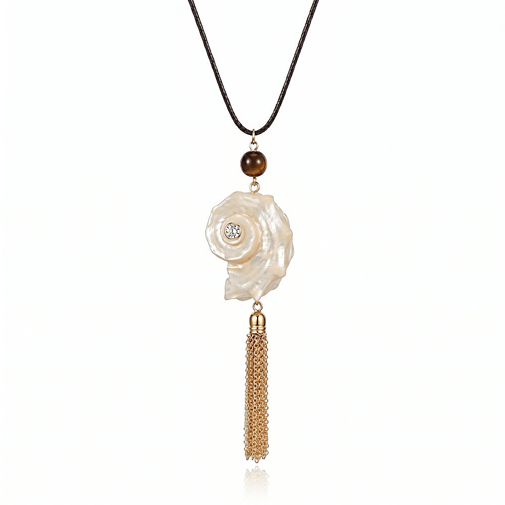 Discover the Siren Shell & Tassel Necklace at The Luxe Maison, featuring a luminous spiral shell pendant, golden tassel, tiger eye accent, and sparkling zircon detail for a bold, ocean-inspired look.