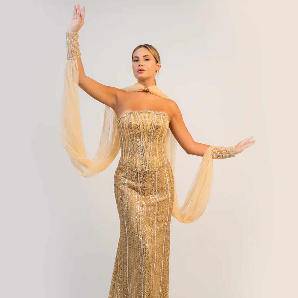 Shop online dazzling gold gown with sparkling corset, sleek silhouette and flowing cape-inspired details, perfect for parties and special occasions.
