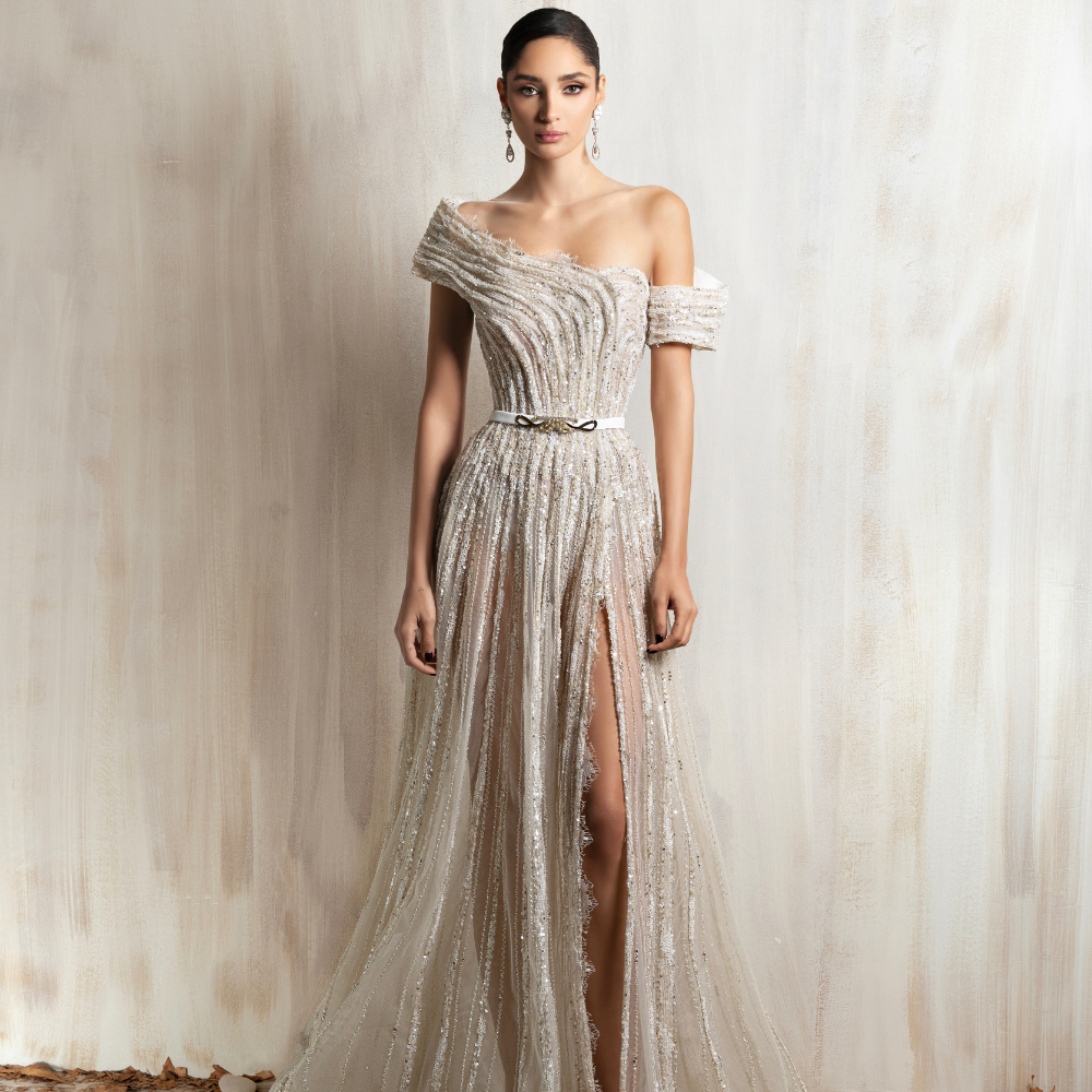 Off-white one-shoulder beaded gown with a high slit, blending elegance and modern glamour. Shop now at our exclusive clothing website.