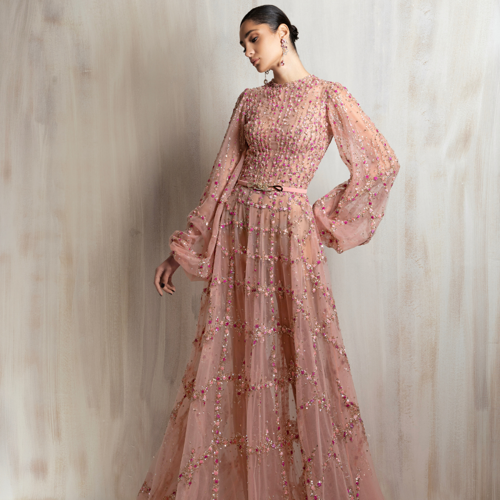 Blush pink beaded tulle gown with sheer long sleeves and a flowing skirt, perfect for elegant occasions. Shop now at our exclusive clothing website.