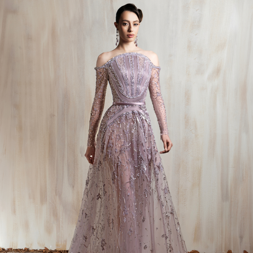 Dusty lavender beaded tulle gown with an off-shoulder neckline and sheer sleeves, perfect for elegant occasions. Shop now at our exclusive clothing website.