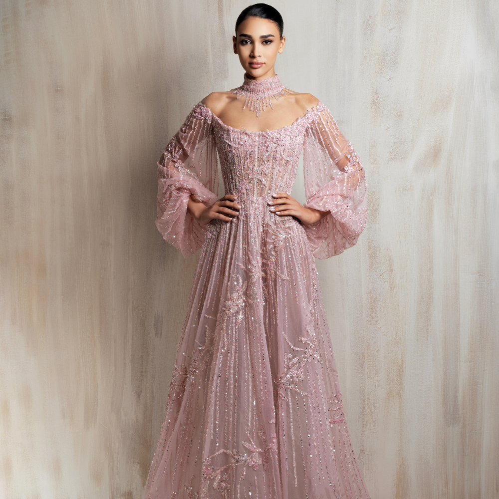 Soft blush pink beaded tulle gown with an off-shoulder neckline and voluminous sleeves. Shop now at our exclusive clothing website.