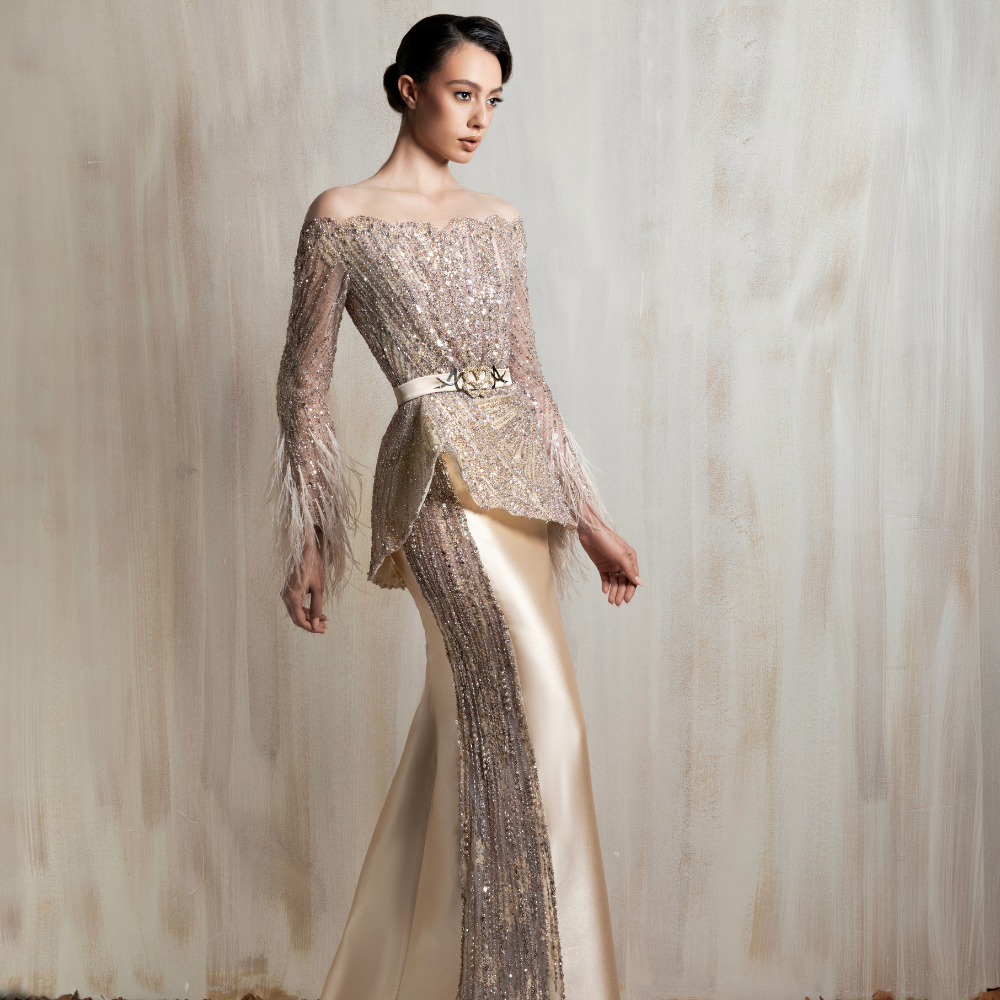Off-shoulder champagne gown with beadwork, feathered sleeves, a peplum bodice, and satin skirt. Shop now at our exclusive clothing website.
