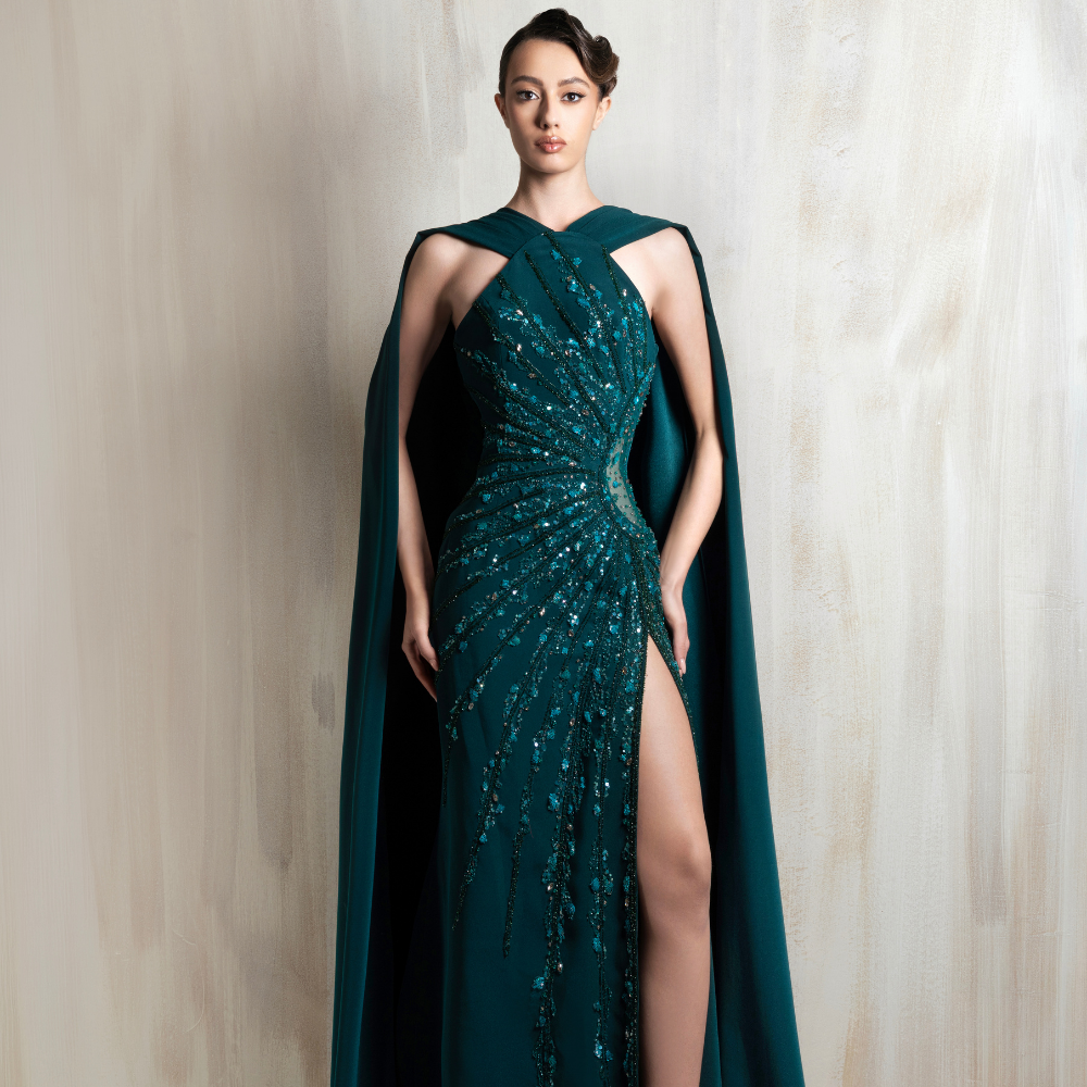 Emerald halter gown with beaded draping and a flowing cape, crafted for elegant evening occasions. Shop now at our exclusive clothing website.