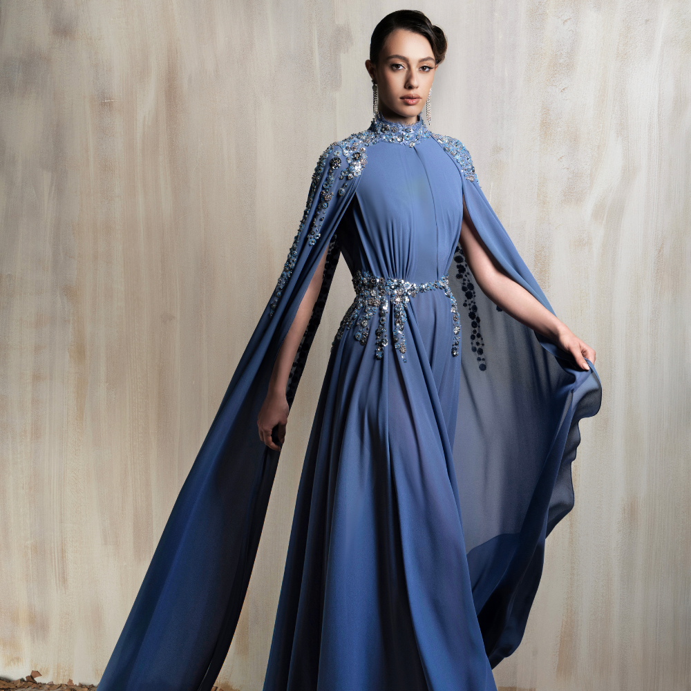 Royal blue cape gown with a crystal-embellished cape, crafted for regal elegance and glamour. Shop now at our exclusive clothing website.