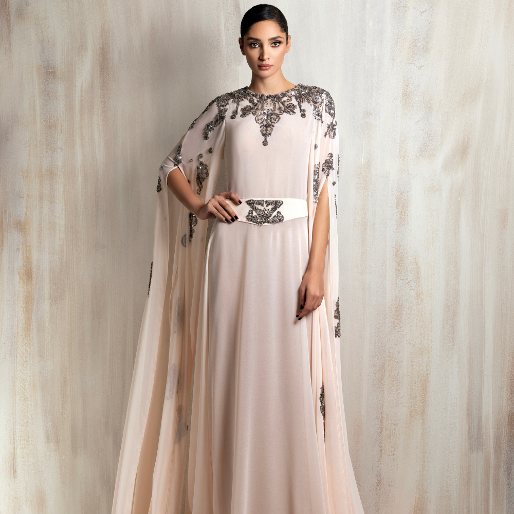 Soft blush cape gown with intricate silver embroidery, designed for timeless elegance. Shop now at our exclusive clothing website.