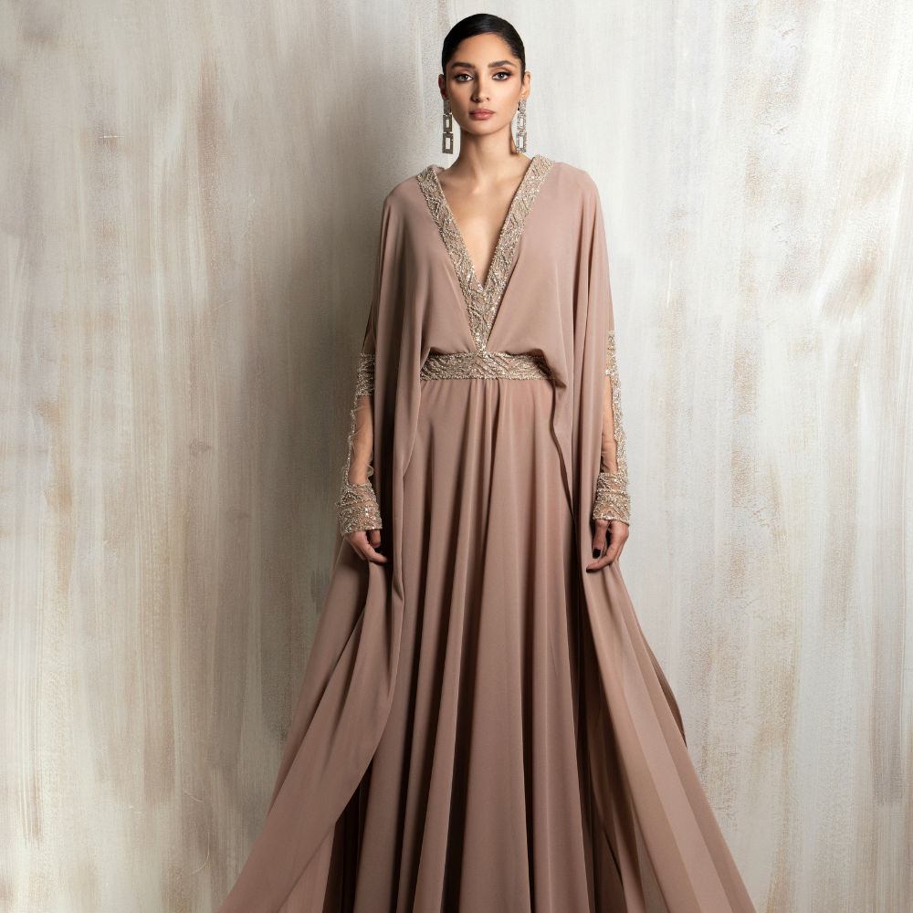 Flowing taupe gown with a gold-embroidered neckline and cape sleeves, designed for elegant occasions. Shop now at our exclusive clothing website.