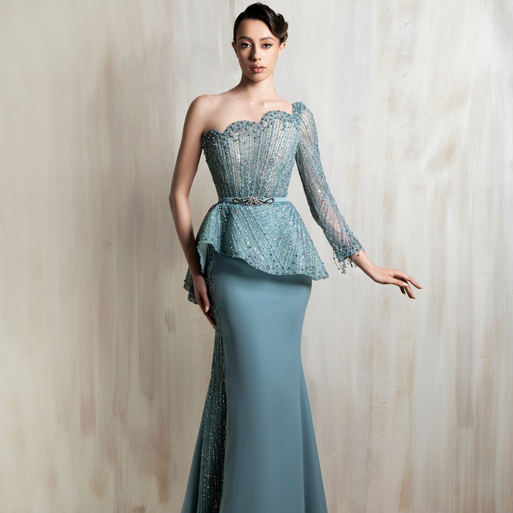 One-shoulder icy blue gown with beaded corset, asymmetric peplum, sheer sleeve, and fitted skirt. Shop now at our exclusive clothing website.