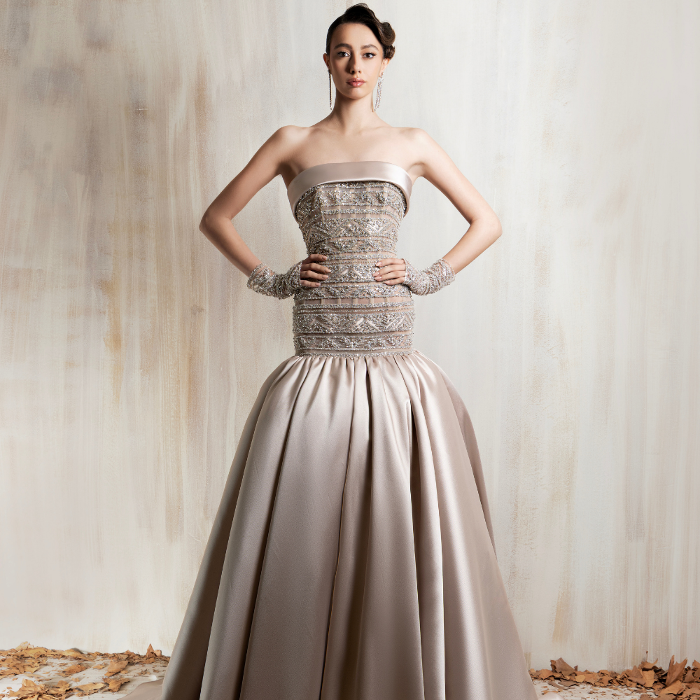 Strapless beige ball gown with a beaded bodice, voluminous satin skirt, and short beaded gloves. Shop now at our exclusive clothing website.