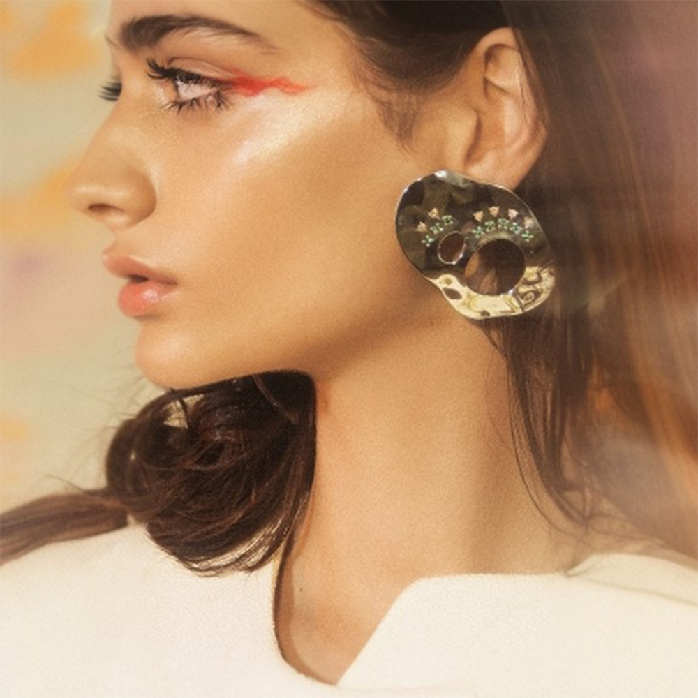Statement earrings embellished with multi colored zircon stones on reflective surface.