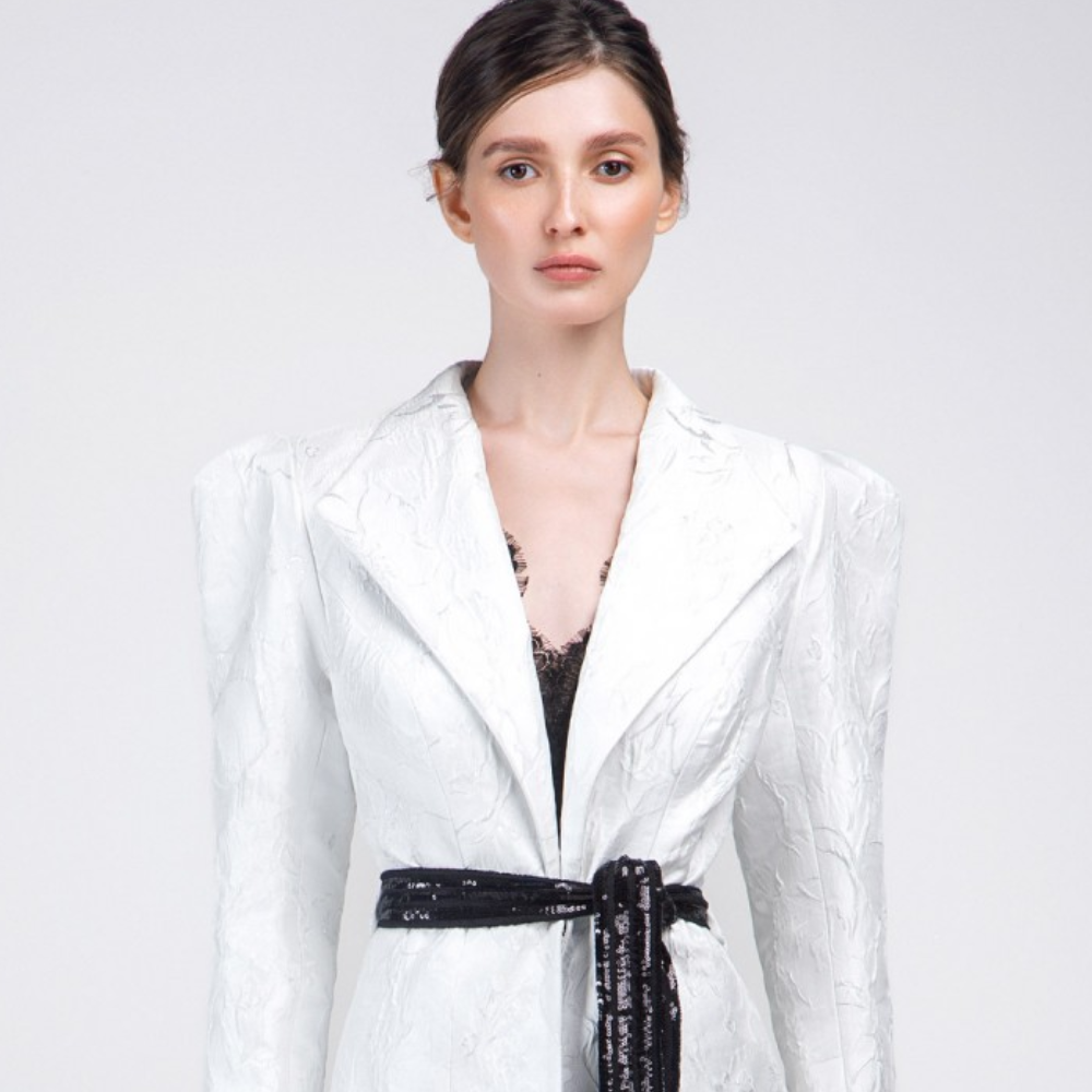 The black lace fabric sleeveless jumpsuit comes with a brocade white color jacket and embroidered black sequins belt.