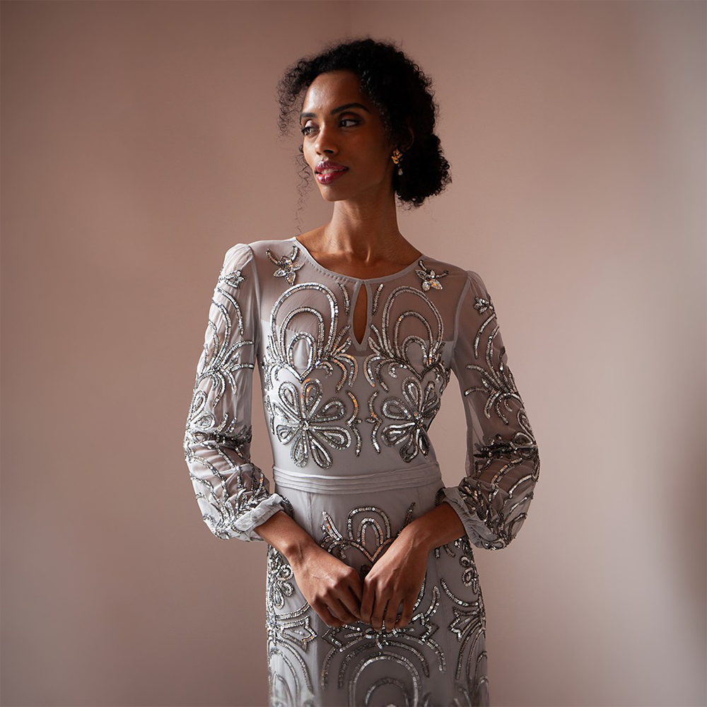 Elevate your look with the breathtaking silver floor-length gown adorned featuring mesh sleeves and a neckline. 