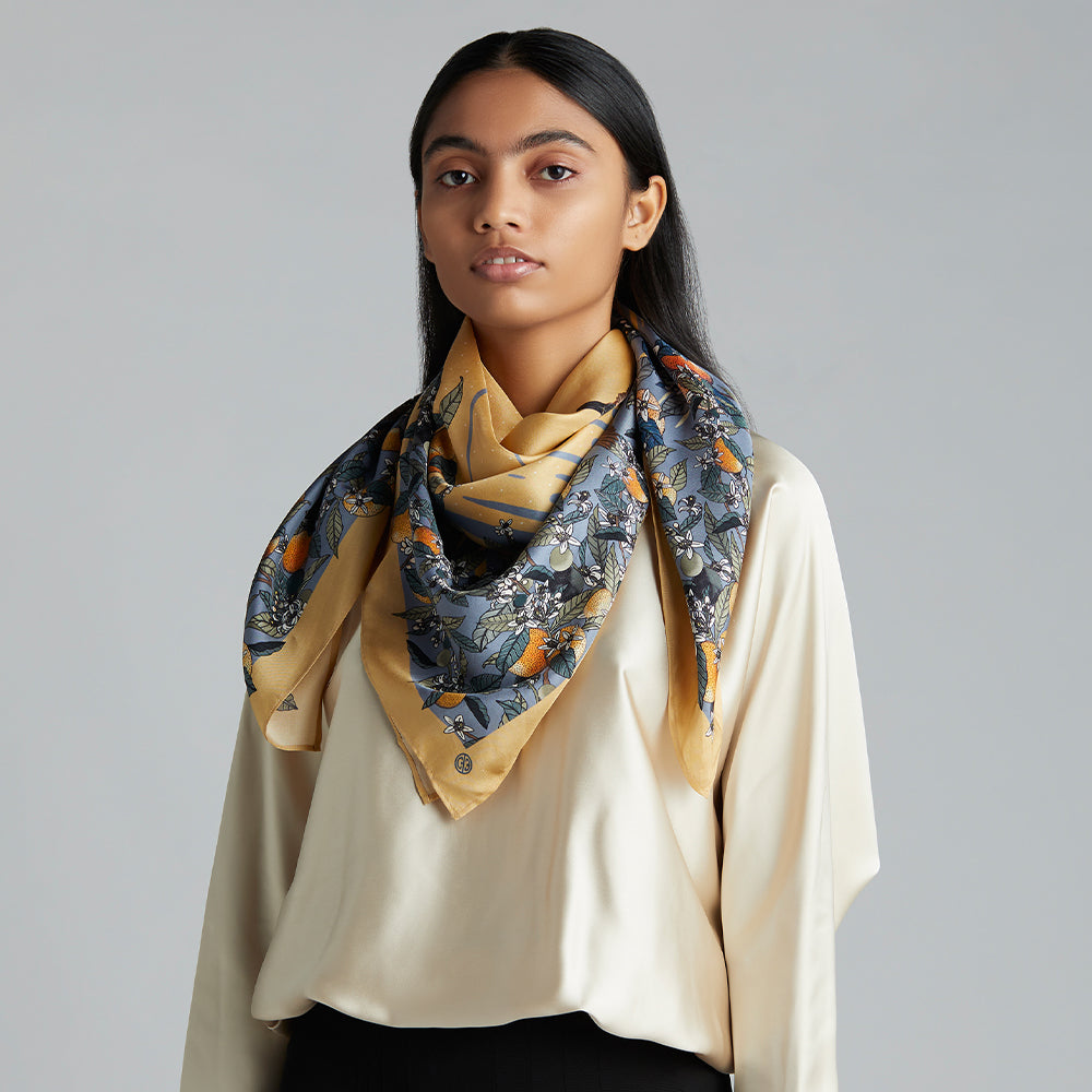 A stonewashed blue scarf with orange blossoms and fruit delicately hand-illustrated, and sparrows hidden under the stems.