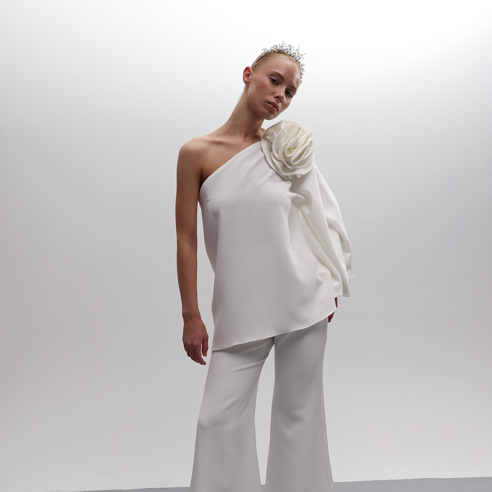 One-shoulder off white top with a sizable matching fabric flower, featuring bell sleeves for sophistication.