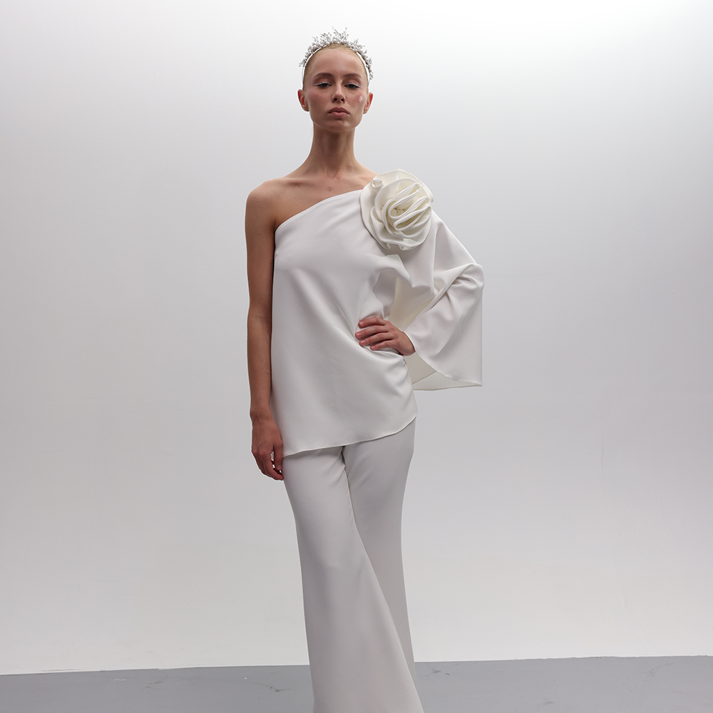 One-shoulder off white top with a sizable matching fabric flower, featuring bell sleeves for sophistication.