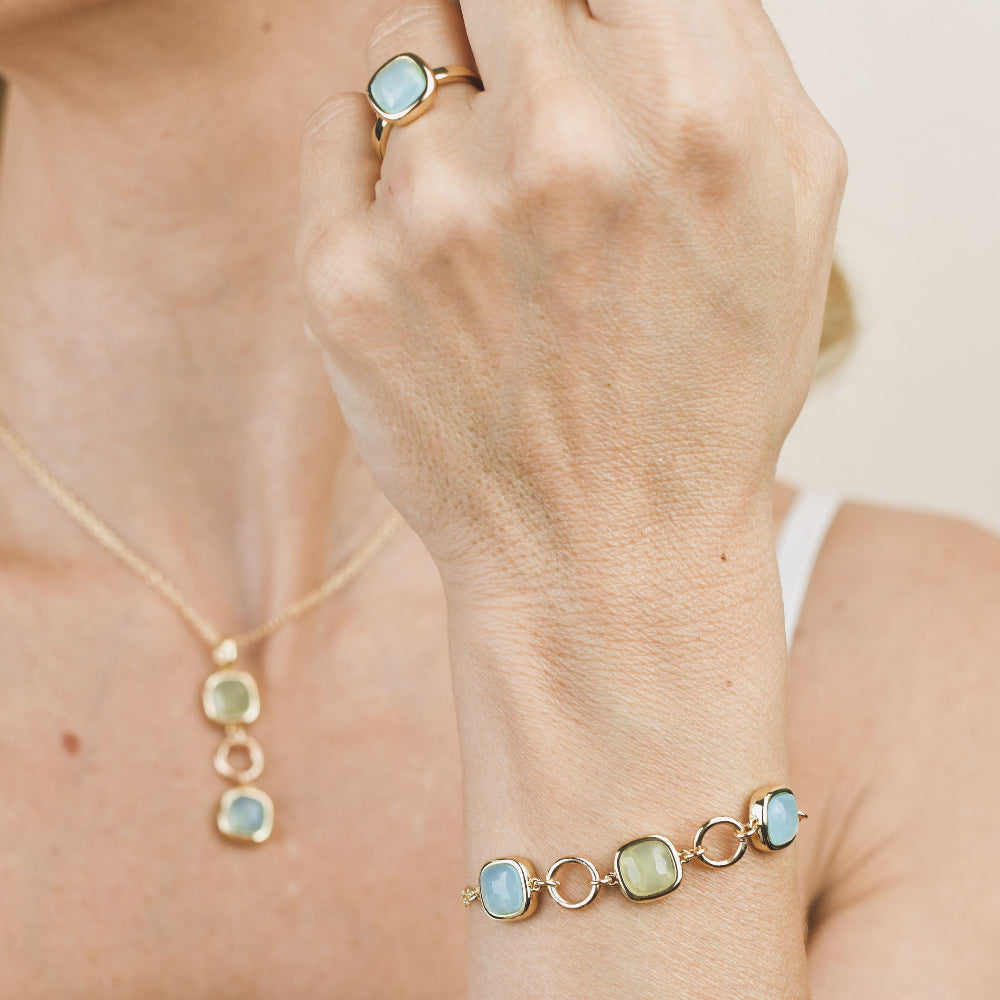 Yellow gold plated bronze bracelet with green and aquamarine crystal accents, detailed with circular gold plated modules for a modern layered look. Shop premium jewelry online.