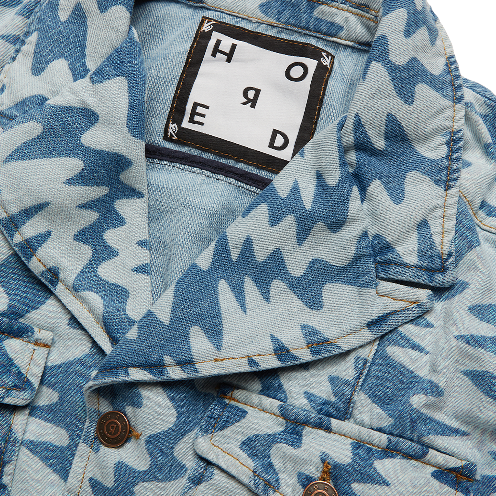 Horde Studio white denim jacket is patterned with cerulean blue wavy motif. It’s crafted from a rigid denim 