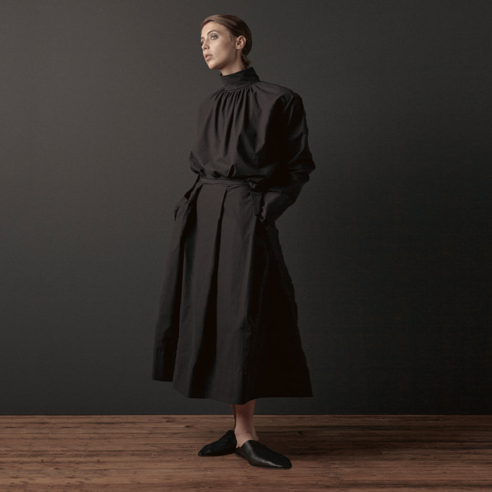 Discover the Ila Skirt at The Luxe Maison, featuring a calf-length silhouette, wide pleats, side pockets, and a narrow waistband with a mother-of-pearl button.