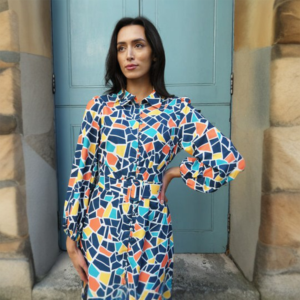 Vibrant blue, yellow and orange geometric print dress has a buttoned front and a buckled belt finished with a pleated hem