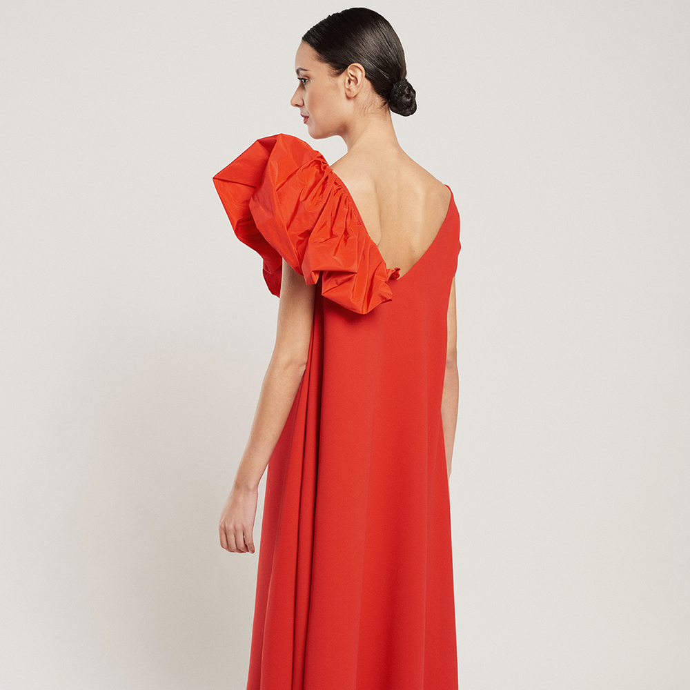 Shop the cape-style red Laura dress in crepe with a red technical fabric ruffle, side pockets and slit at the front. Shop now!