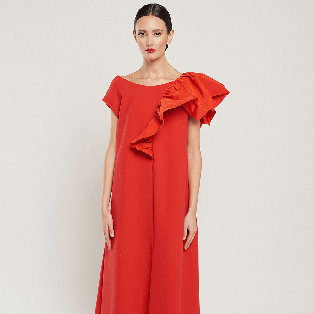 Shop the cape-style red Laura dress in crepe with a red technical fabric ruffle, side pockets and slit at the front. Shop now!